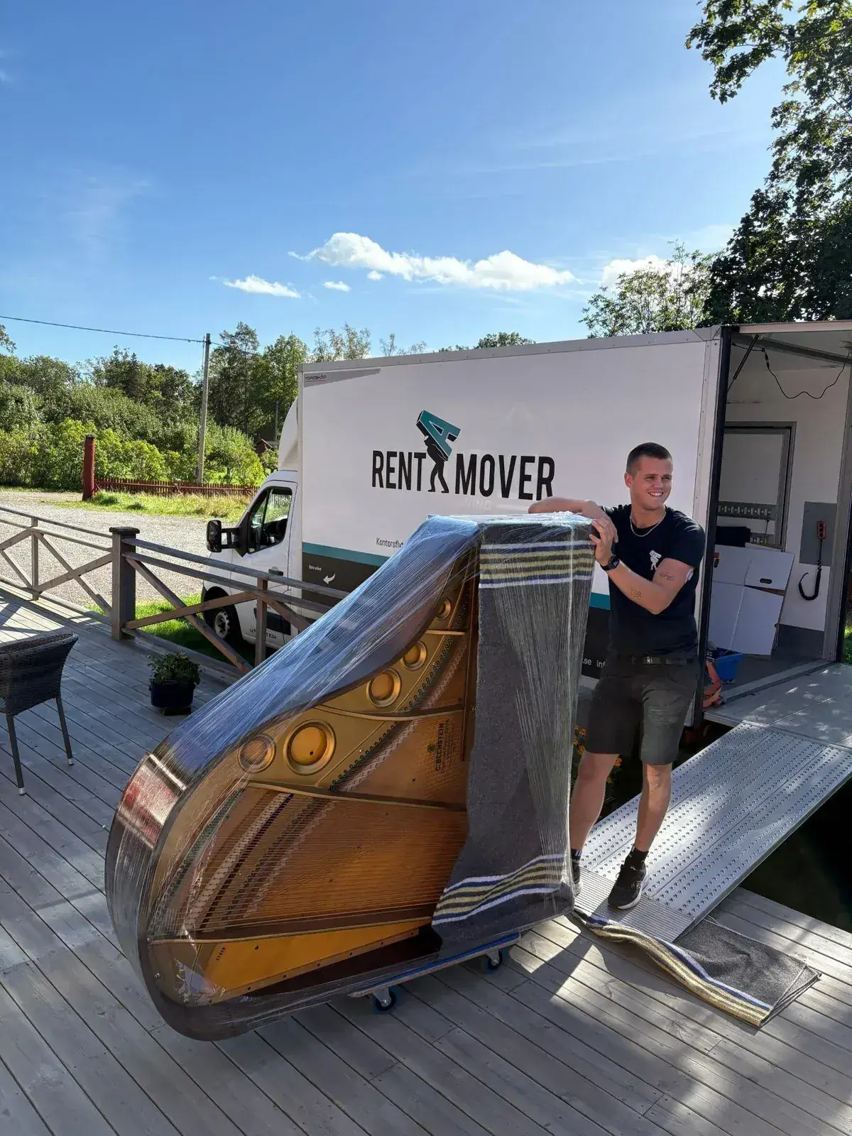 Pianoflyttare från Rent A Mover lastar ett inplastat flygel på pianokärra vid flyttbilen i Stockholm.
